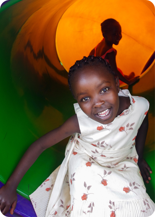 Smiling child playing on a colorful indoor playground slide with another child inside the play tunnel